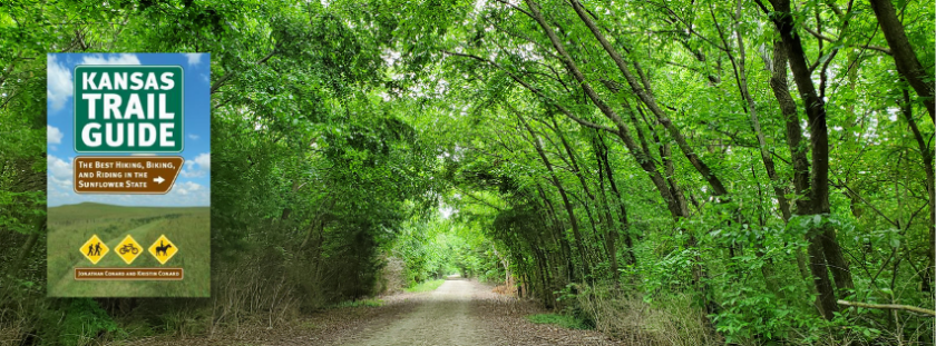 Green-leafed trees arch over a gravel trail. A book cover for Kansas Trail Guide is highlighted on the left.