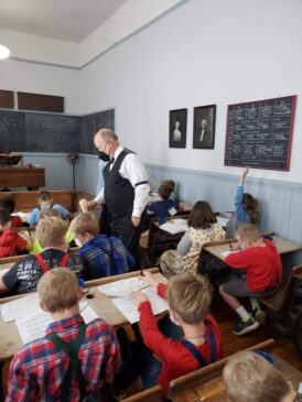 A man in turn-of-the-century clothing walks among students sitting at desks