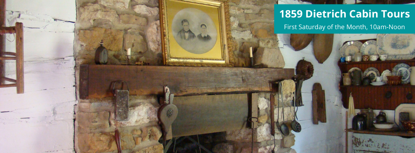 Image shows a stone fireplace. A large gold-framed wedding photo of a couple rests on a mantel. The fireplace is surrounded by household items common in the 1800s. Text reads 1859 Dietrich Cabin Tours First Saturday of the Month, 10 am to Noon