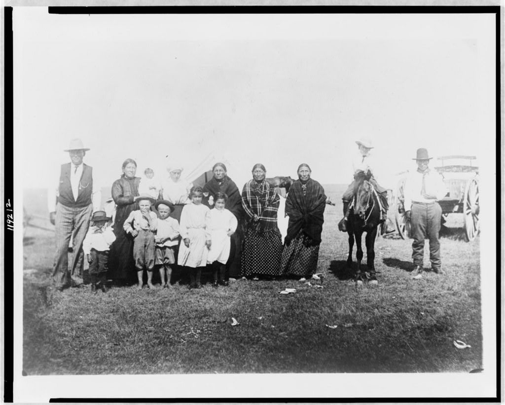 Group of Kickapoo Indians, standing outside tent, dressed in Euro-American clothing