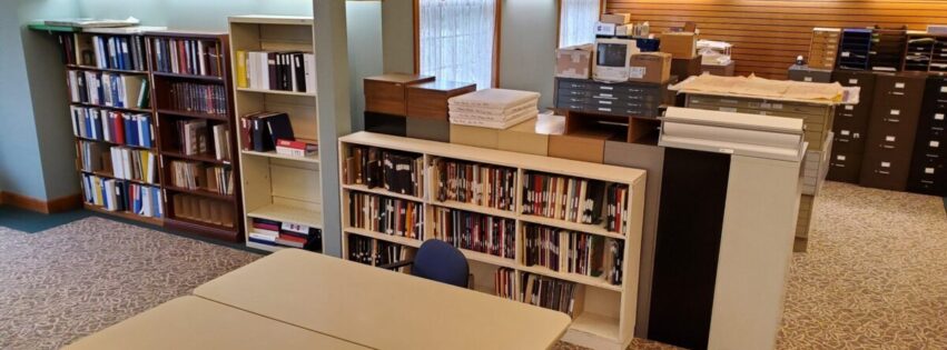 Bookcases filled with books. Tables and chairs. File cabinets. Large prints of historic photos in the background.