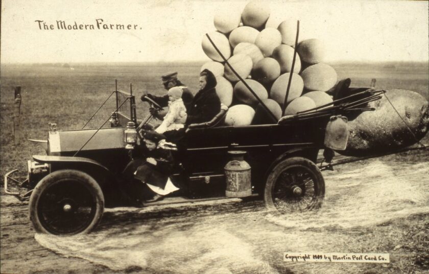 Man and woman sit in an early 1900s automobile. Gigantic eggs fill the back seat and a large potato is strapped to the back. Two children hang from the side.