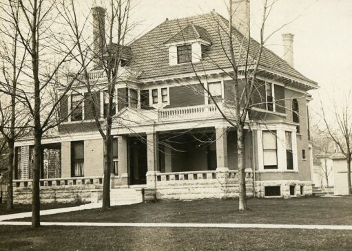 Historic photo of a 2 1/2 story Italian Renaissance Revival house with a red tile roof, brick first floor, and large wrap-around porch.