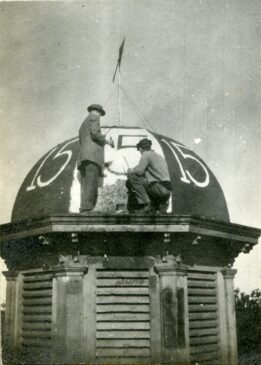 Two mail students are painting "1915" on a dome on top of a building.